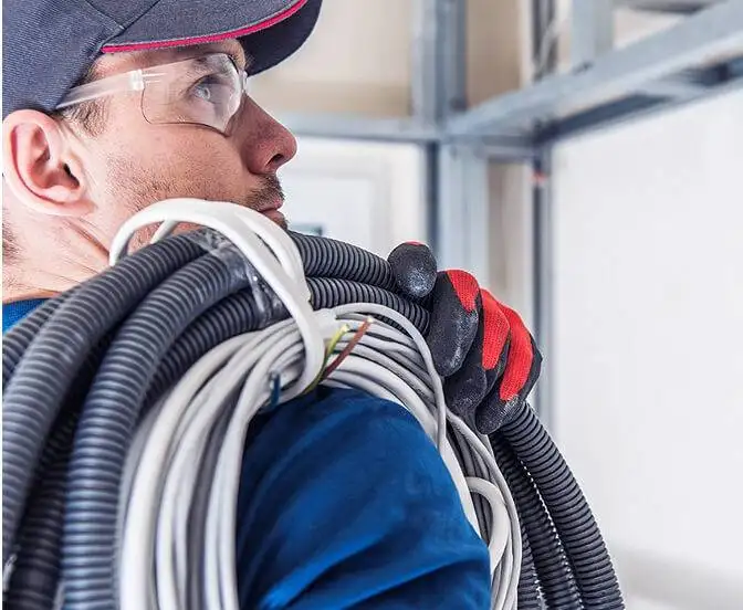 Electrician carrying coiled cables on shoulder looks thoughtfully in the distance.