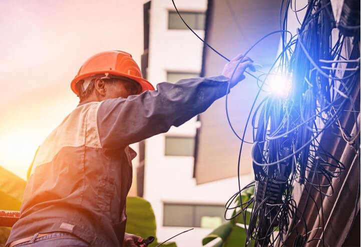 An electrician in a hard hat working on tangled cables outdoors at dusk.