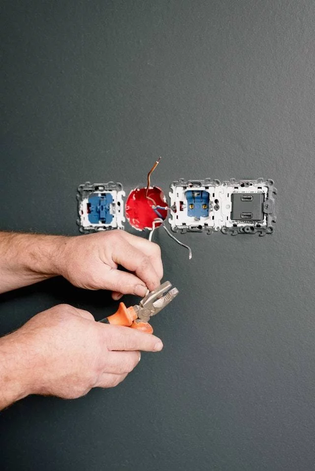 An electrician is installing a new electrical outlet on a gray wall.