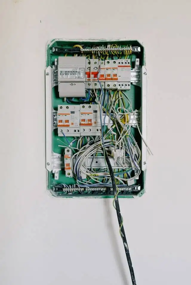 Open electrical distribution box with wires and circuit breakers on a wall.