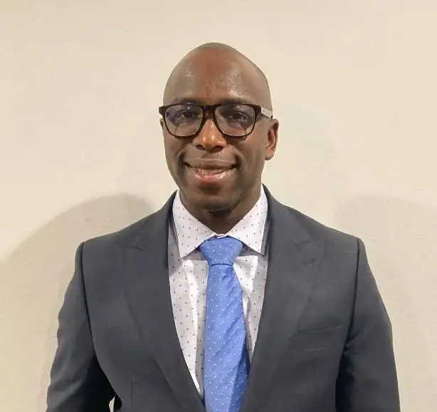 A man in a suit and tie with glasses smiling at the camera.